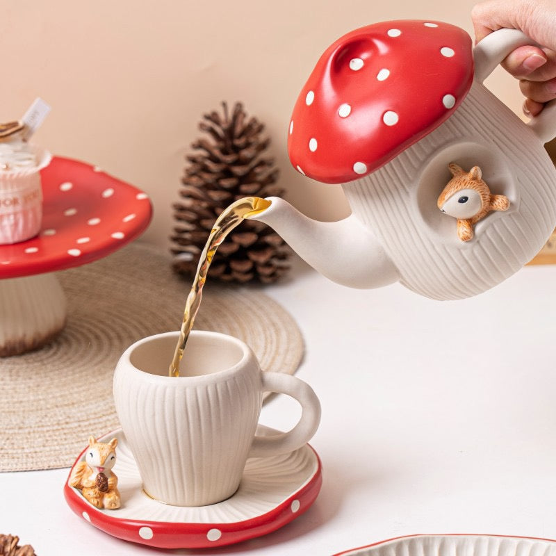 Red mushroom ceramic teapot pouring tea into matching cup and saucer